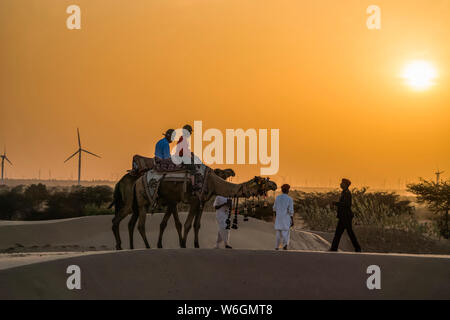 People riding with camels in the desert at sunset; Rajasthan, India Stock Photo