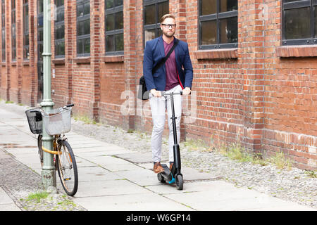 A Young Businessman With Shoulder Bag Riding An Electric Scooter On Street Stock Photo