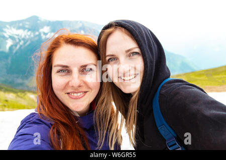 Selfie time. Two girls take a picture with their mobile. Two friends enjoy nature and the outdoors on the side of the mountain Stock Photo
