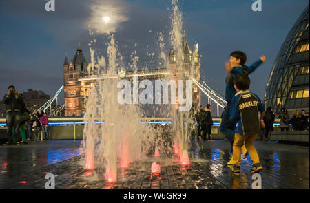 City Hall, South Bank, London, UK. 23rd December, 2015. Children dart in and out of the water feature next to City Hall in London with Tower Bridge in Stock Photo