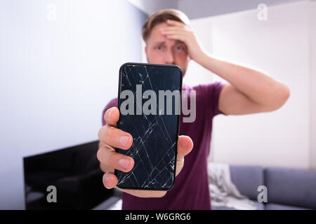 Worried Man Holding Broken Smartphone At Home Stock Photo