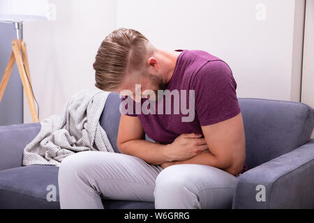 Young Man Suffering From Stomach Pain Sitting On Sofa At Home Stock Photo