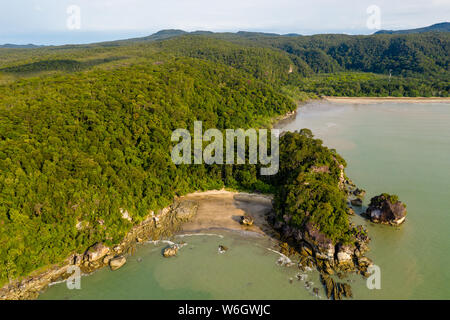 Aerial drone view of a beautiful small, deserted sandy beach in a small bay surrounded by tropical rainforest Stock Photo