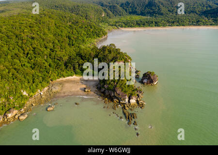 Aerial drone view of a beautiful small, deserted sandy beach in a small bay surrounded by tropical rainforest Stock Photo