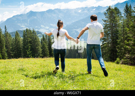 Couple Holding Hands Running On Field In Mountains Stock Photo