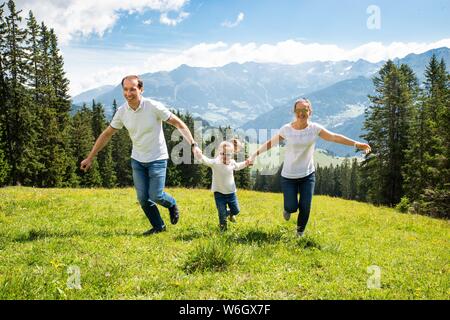Family With Daughter Holding Hands Running On Field In Mountains Stock Photo