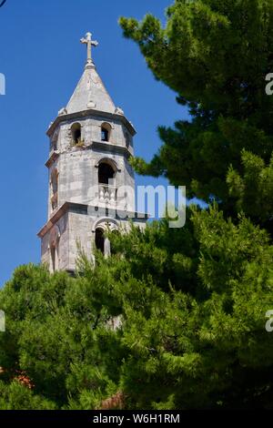 Grey steeple under a blue sky behind pines Stock Photo