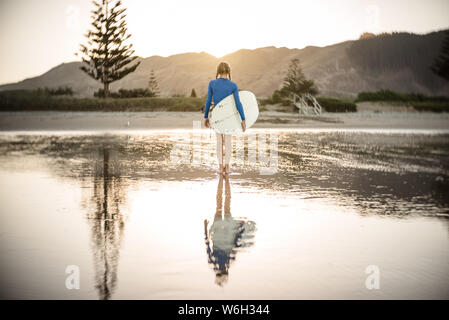 Tween girl on New Zealand beach holding surfboard