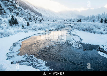 River flowing through a snowy, mountainous landscape at sunrise; Alaska, United States of America Stock Photo