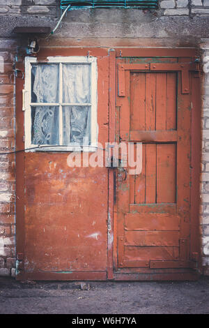 Facade of an old building with red door on lock and small white window with curtain. Stock Photo