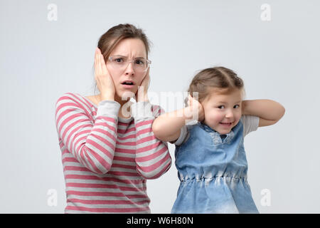 woman and her little daughter cover ears with hands. Avoid loud noise. Stock Photo