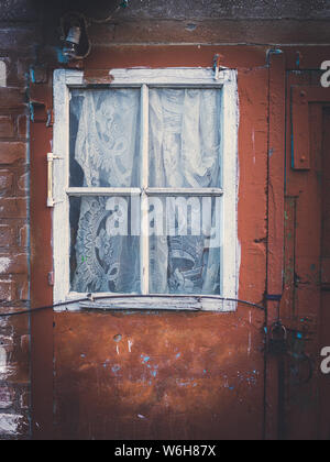 Facade of an old building, red wall with white window and curtain. Stock Photo