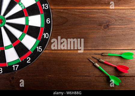 Darts target isolated on a wooden background and three color darts. Hit the target. Stock Photo