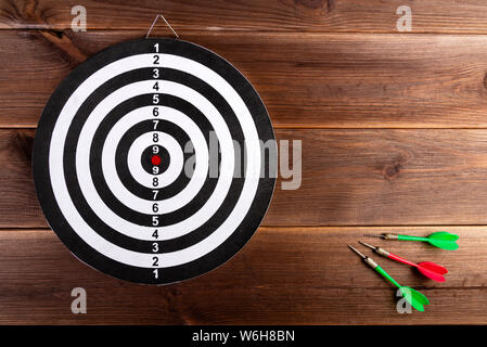 Darts target isolated on a wooden background and three color darts. Hit the target. Stock Photo