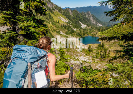Female backpacker on High Divide Trail looking down at Round Lake in summertime, Seven Lakes Basin, Olympic National Park, Olympic Mountains Stock Photo