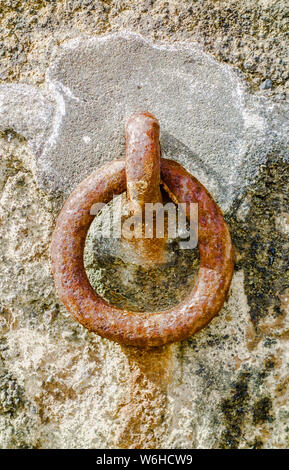 Rusted steel mooring ring attached to cement on rock wall. Stock Photo