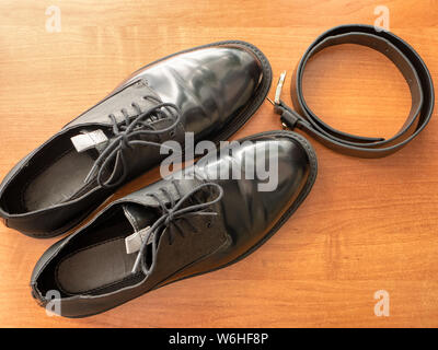 pair of elegant glossy black formal man shoes and leather belt on wooden table Stock Photo