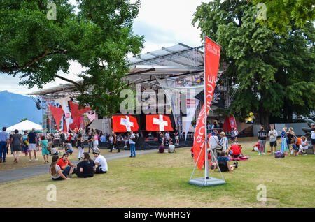 Vevey, Switzerland - Aug 1 2019: People celebrating Swiss National Day in park. Celebration of the founding of the Swiss Confederacy. Independence day. Switzerland flags decoration, screens. Stock Photo