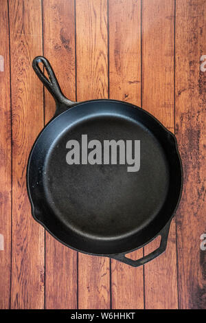 Traditional heavy duty cast iron skillet on wooden surface - isolated top view with copy space. Black cooking utensil - campfire cookware and kitchenw Stock Photo