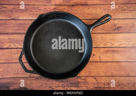 Traditional heavy duty cast iron skillet on wooden surface - isolated top view with copy space. Black cooking utensil - campfire cookware and kitchenw Stock Photo