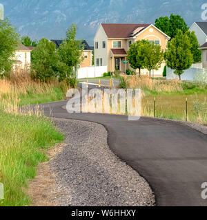 Square Road winding amid grassy terrain with homes trees and mountain in the distance Stock Photo