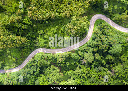 Aerial view over mountain road going through tropical rainforest landscape in Thailand. Stock Photo