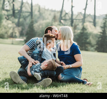 A family with young children playing in a park, with the mother and father kissing; Edmonton, Alberta, Canada