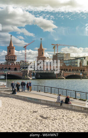 BERLIN, GERMANY - September 26, 2018: Panorama of Berliners sitting by the Spree river, near the East Side Gallery with the Oberbaum Bridge in the Stock Photo