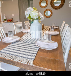Square Table runner flowers glasses napkins and plates arranged on top of dining table Stock Photo