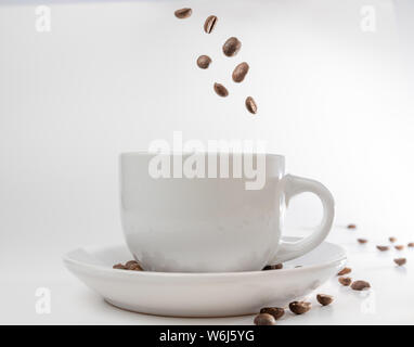 Coffee beans fall into a white porcelain cup and saucer, bouncing and jumping through the air conveying alert excitement, all isolated against a white Stock Photo