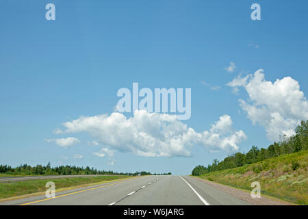 Blue sky and puffy clouds against an empty open highway in the summer Stock Photo