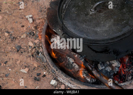 Coals and flames on a fire pit with a black cauldron oven Stock Photo