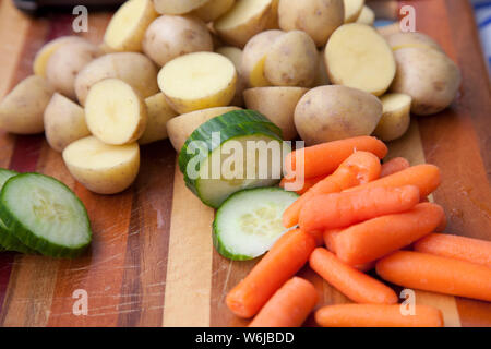 Freshly cut carrots, potatoes and cucumbers on a wooden board Stock Photo