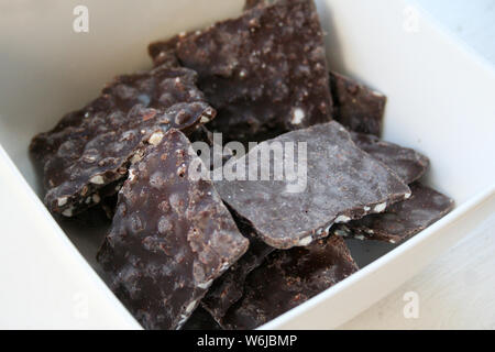 Tasty looking thin slivers of chocolate bark with nuts inside a white bowl Stock Photo