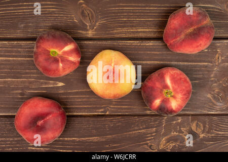 Group of five whole fresh red peach prunus persica platycarpa flatlay on brown wood Stock Photo