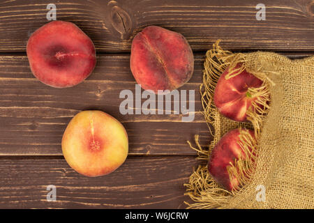 Group of five whole fresh red peach prunus persica platycarpa on natural sackcloth flatlay on brown wood Stock Photo
