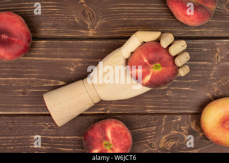 Group of five whole fresh red peach prunus persica platycarpa in wooden hand flatlay on brown wood Stock Photo