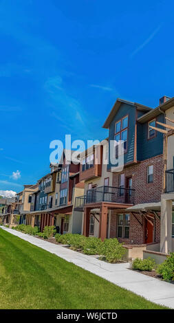 Vertical Row of homes with porches and small balconies under blue sky on a sunny day. A paved pathway and grassy terrain can be seen in front of the r Stock Photo