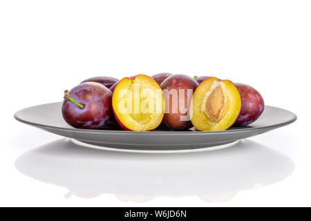 Group of lot of whole two halves of fresh blue plum with a stone on a gray ceramic plate isolated on white background Stock Photo