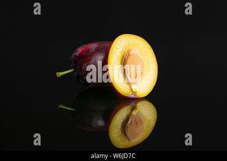 Group of one whole one half of fresh blue plum with a stone isolated on black glass Stock Photo