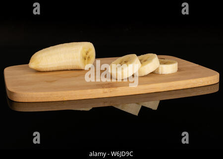 Peeled one half three slices of ripe yellow banana on bamboo cutting board isolated on black glass Stock Photo