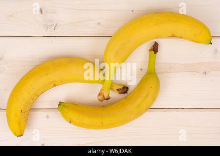 Group of three whole ripe yellow banana placed diagonally flatlay on white wood Stock Photo