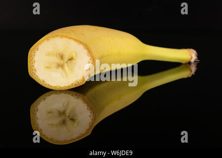 One half of ripe yellow banana isolated on black glass Stock Photo