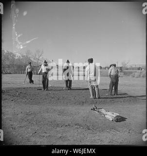 Manzanar Relocation Center, Manzanar, California. Golfing enthusiasts enjoy a friendly game of golf . . .; Scope and content:  The full caption for this photograph reads: Manzanar Relocation Center, Manzanar, California. Golfing enthusiasts enjoy a friendly game of golf at the Manzanar Golf Course. These golfers, and other fellow evacuees, when clearing the brush and constructing their own course, took advantage of the natural topography in laying out the nine holes. As can be seen, all greens are sand, rather than turf. Stock Photo