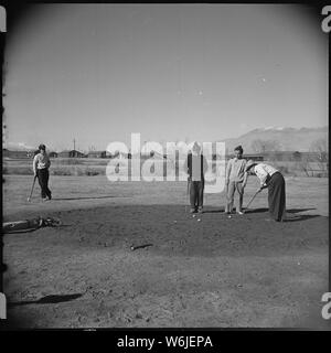 Manzanar Relocation Center, Manzanar, California. Golfing enthusiasts enjoy a friendly game of golf . . .; Scope and content:  The full caption for this photograph reads: Manzanar Relocation Center, Manzanar, California. Golfing enthusiasts enjoy a friendly game of golf at the Manzanar Golf Course. These golfers, and other fellow evacuees, when clearing the brush and constructing their own course, took advantage of the natural topography in laying out the nine holes. As can be seen, all greens are sand, rather than turf. Stock Photo