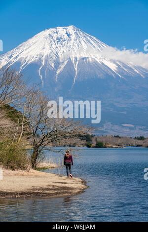 Young woman on the shore, view over a lake to the volcano Mt Fuji, Tanuki Lake, Yamanashi Prefecture, Japan Stock Photo