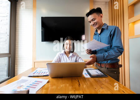 Young Asian business colleagues in team casual discussion, startup project business meeting or happy teamwork. Two analysts discussing online data in Stock Photo