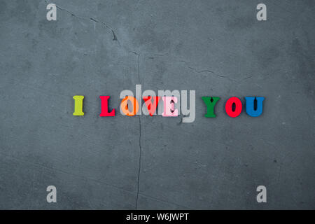 The multicolored I love you word is made of wooden letters on a grey plastered wall background Stock Photo