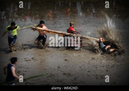 Chinese villagers of the Hakka people carrying a golden statue of ancient Chinese general Guan Gong dash through waterlogged fields during a mud-spatt Stock Photo