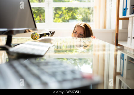 Close-up Of Afraid Businesswoman Hiding Behind The Desk With Laptop Stock Photo